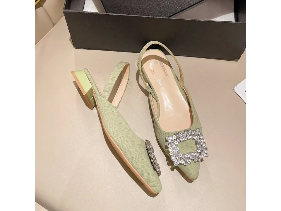 A pair of light green slingback heels with rhinestone buckles displayed on a surface.