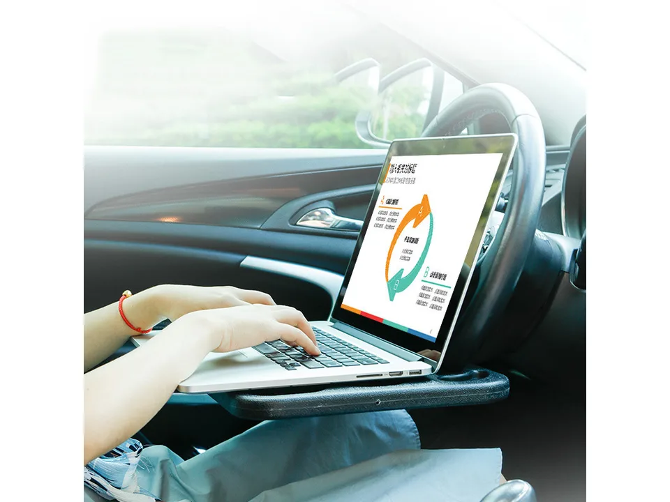 A person using a laptop on a car steering wheel tray.