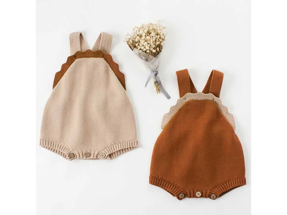 Two baby knit rompers in beige and brown with a small bouquet of flowers.