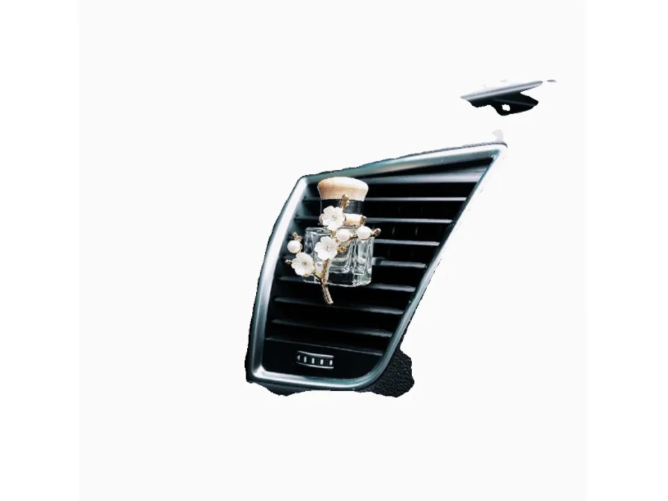Close-up of a car air freshener bottle with a white flower and pearl ornament clipped to a vent.