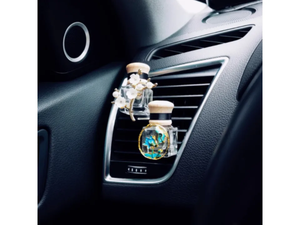 Two decorative car air freshener bottles with floral ornaments clipped onto a car air vent.