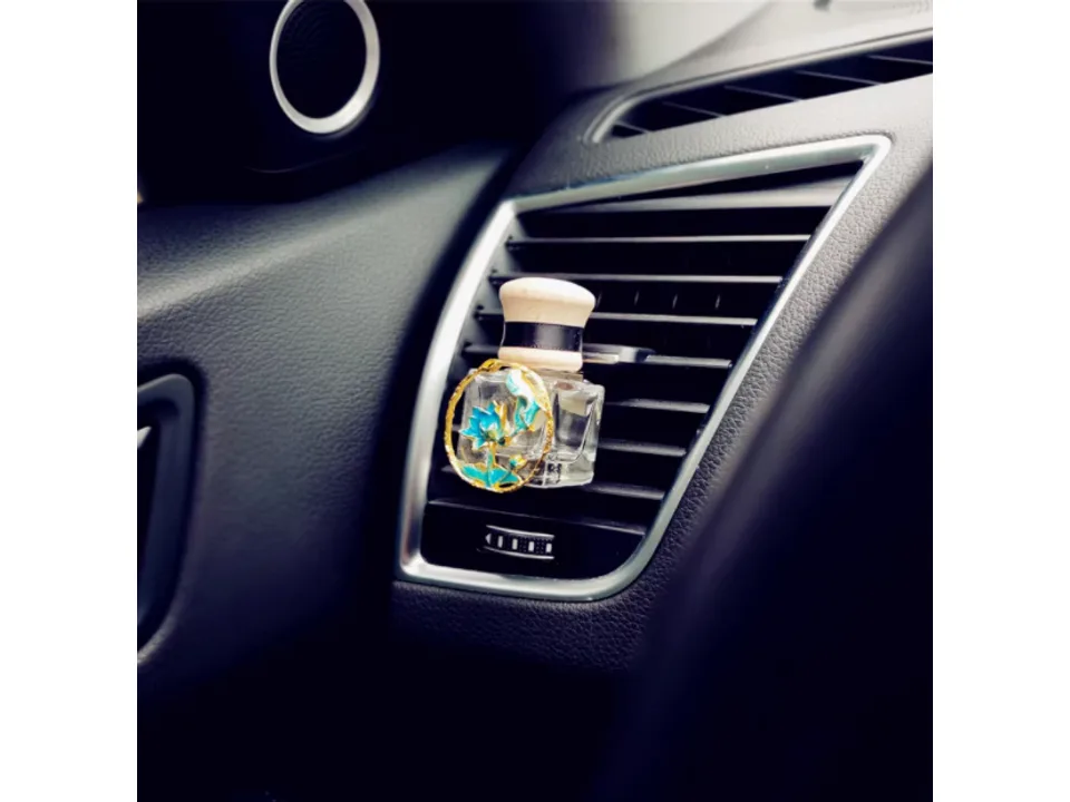 Close-up of a car air freshener bottle with a blue flower ornament clipped to a vent.