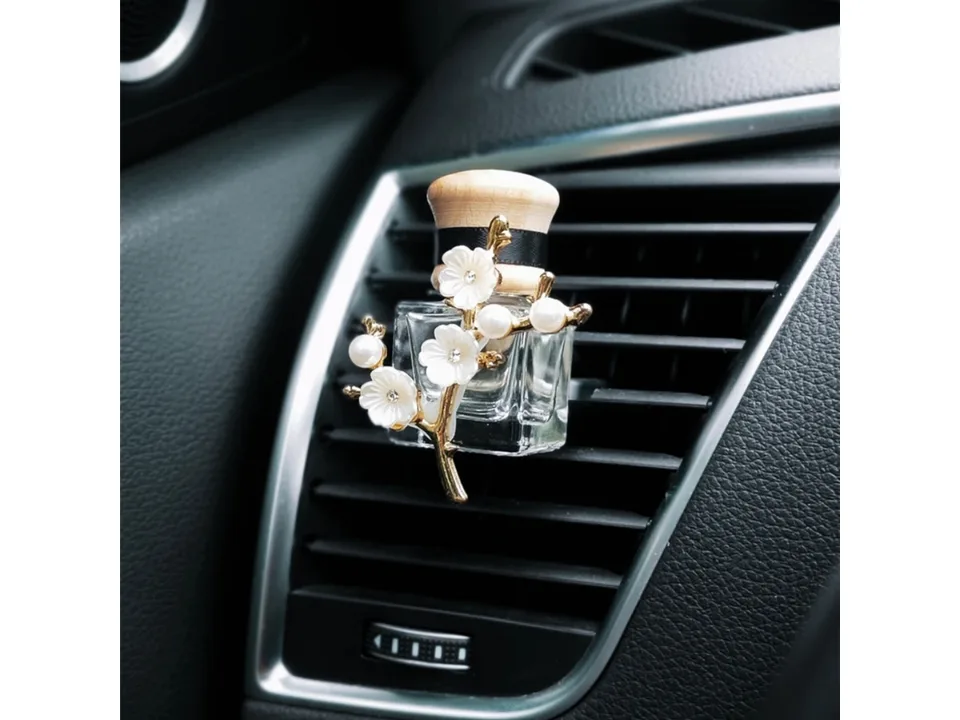 Detailed view of the white flower and pearl car air freshener bottle clipped to a vent.