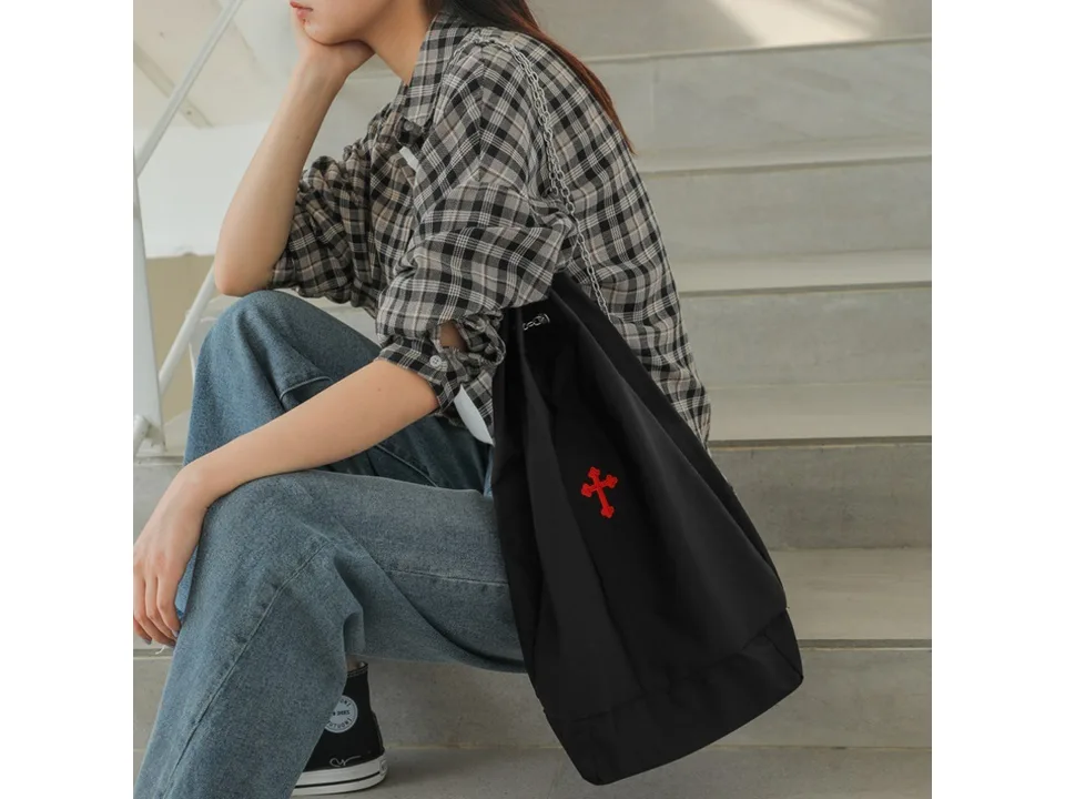 Black drawstring bag with a red cross embroidery being worn over the shoulder.