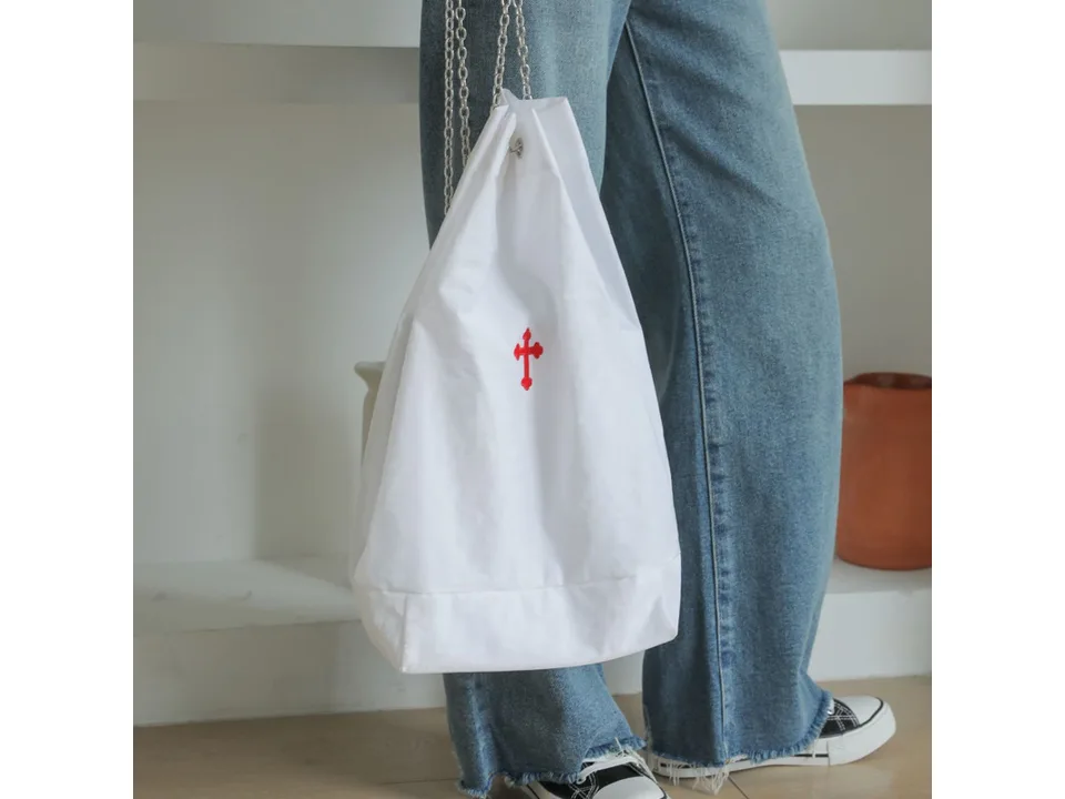 White drawstring bag with a red cross embroidery being worn over the shoulder.