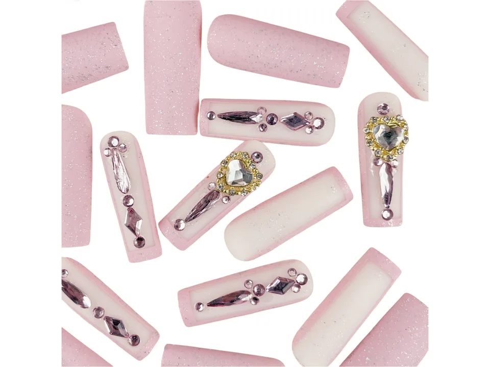 Close-up of several long square press-on nails with pink glitter and rhinestone heart designs.