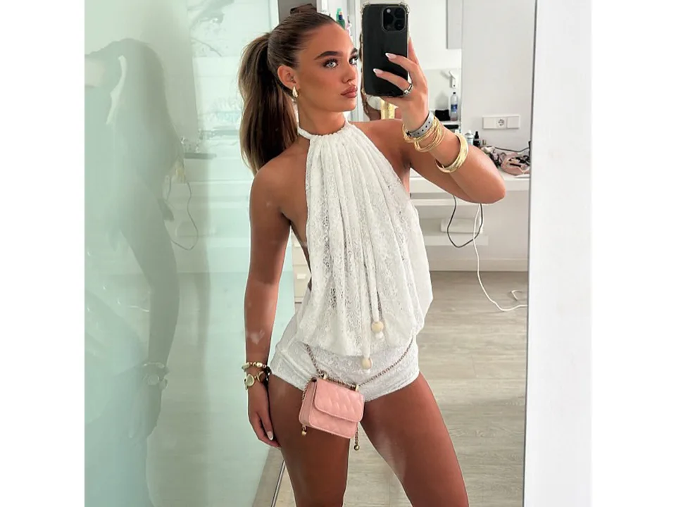 Mirror selfie of a woman wearing a white lace halter jumpsuit with a small pink purse.