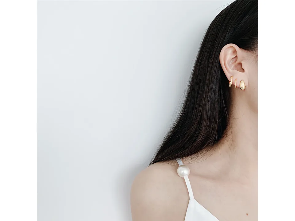 A model wearing three different gold-tone earrings in her earlobe.