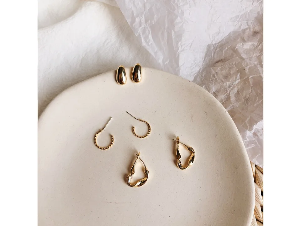 A set of gold-tone earrings including studs and hoops arranged on a ceramic plate.