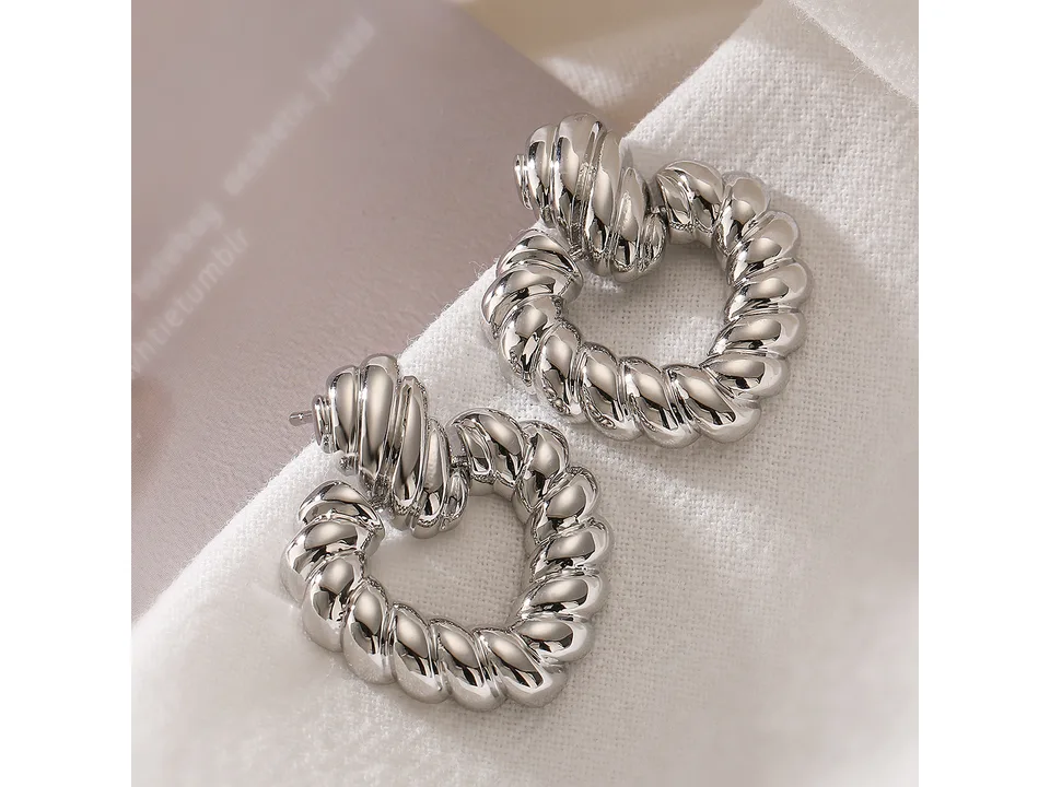 Close-up of silver-tone twisted heart hoop earrings resting on white fabric.