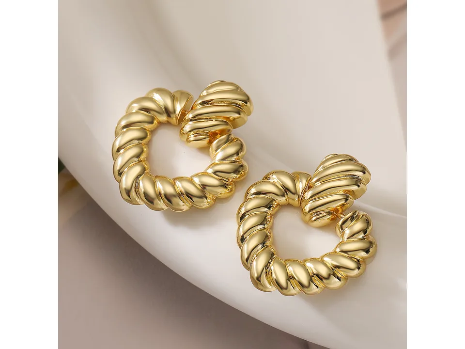 A pair of gold-tone twisted heart hoop earrings on a white surface.
