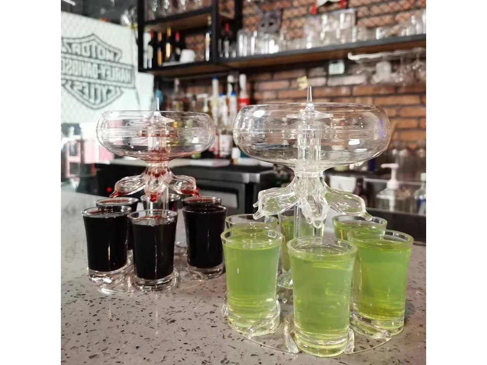 Two shot glass dispensers on a bar counter, one filled with red liquid and one with green liquid.