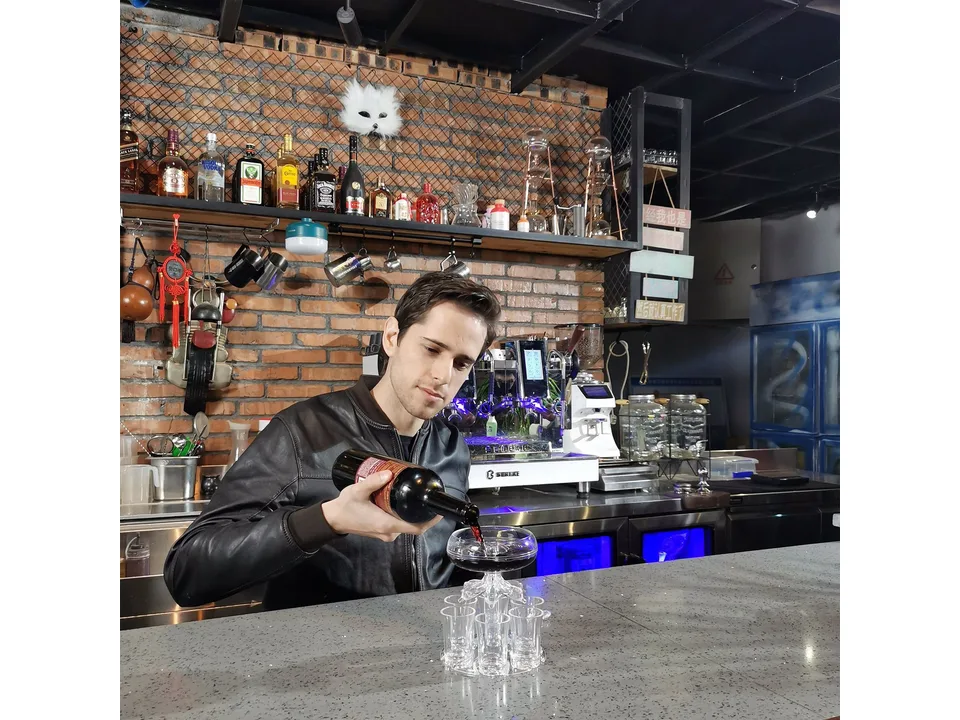 A bartender pouring liquid into the top of the shot glass dispenser.