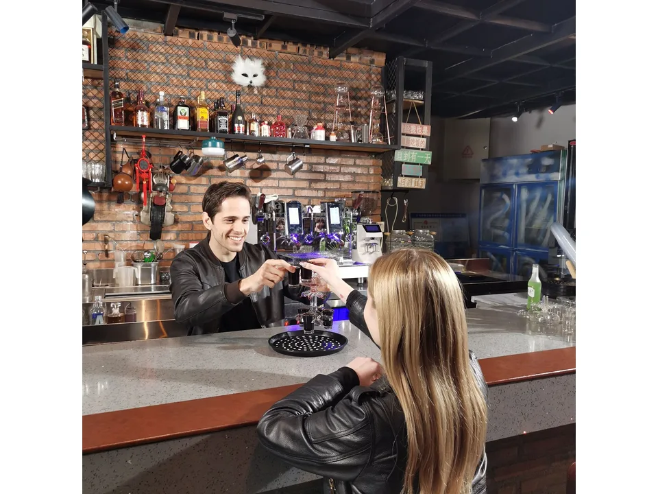 A bartender and a customer toasting with shot glasses from the dispenser.