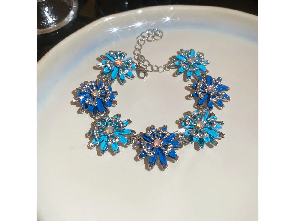 A silver bracelet with blue flower-shaped charms and clear stones on a white plate.