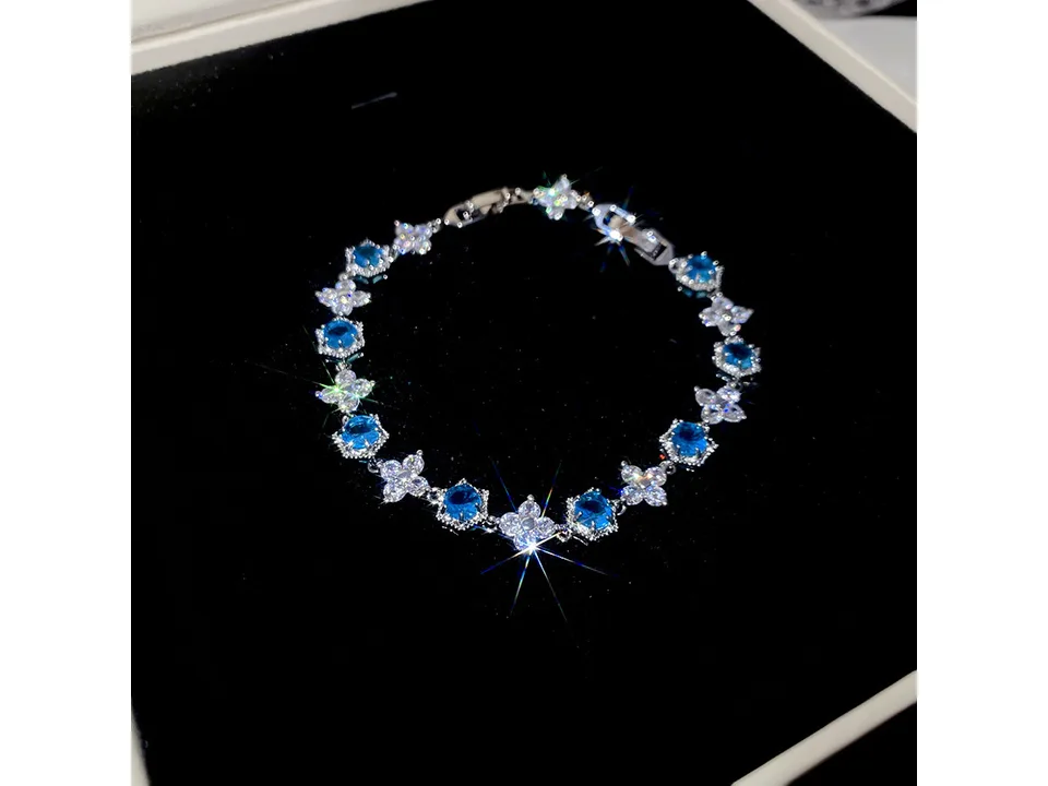 A silver bracelet with blue and clear cubic zirconia stones on a black background.