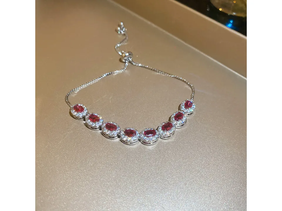A silver adjustable bracelet with red oval stones surrounded by clear crystals.