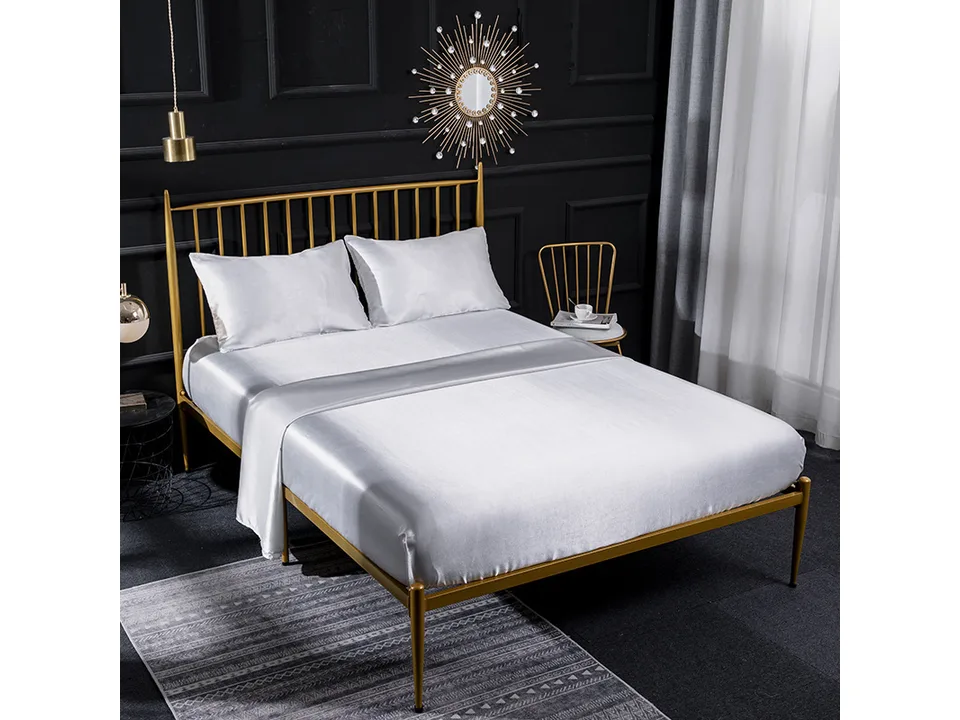 White silk satin bed sheet set on a bed with a gold frame.