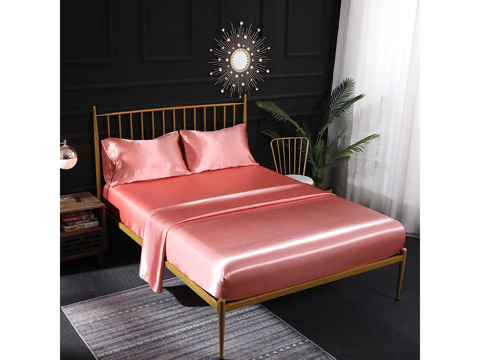 Pink silk satin bed sheet set on a bed with a gold frame.