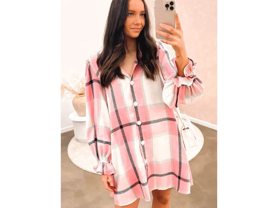 A woman wearing a pink plaid shirt dress with long sleeves and ruffle cuffs.