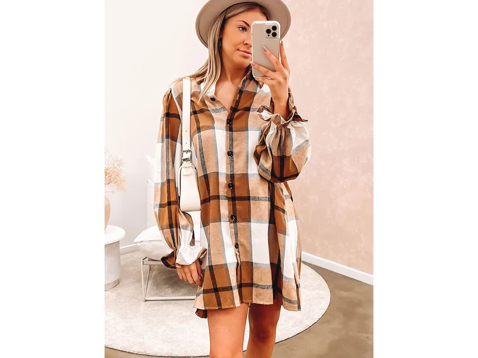 A woman wearing a brown plaid shirt dress with long sleeves and ruffle cuffs.