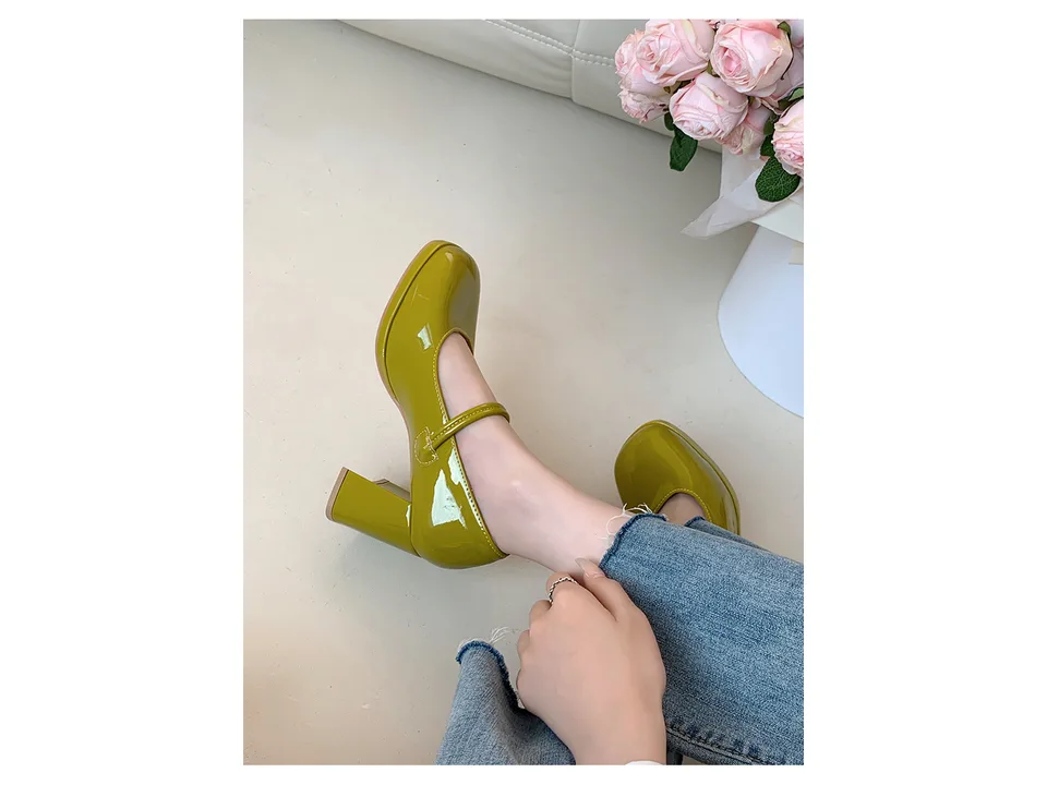 A pair of olive green square toe chunky heel pumps with a buckle strap worn with jeans.