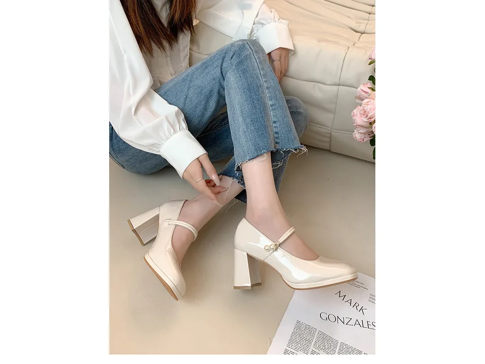 A pair of beige square toe chunky heel pumps with a pearl buckle strap worn with jeans.