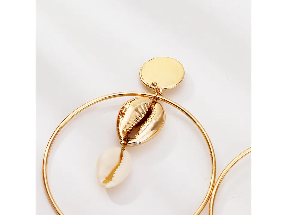 Close-up of a gold hoop earring featuring a metallic shell and a natural shell charm.