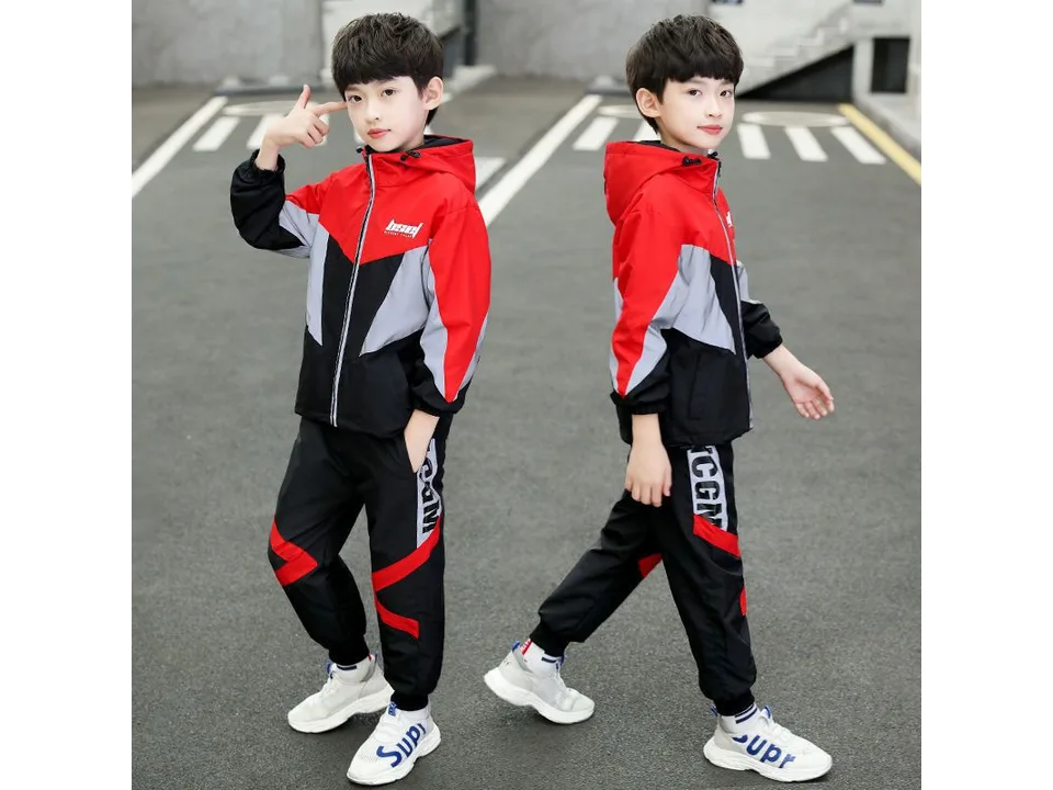 A boy wearing a red, grey, and black hooded jacket and matching trousers.