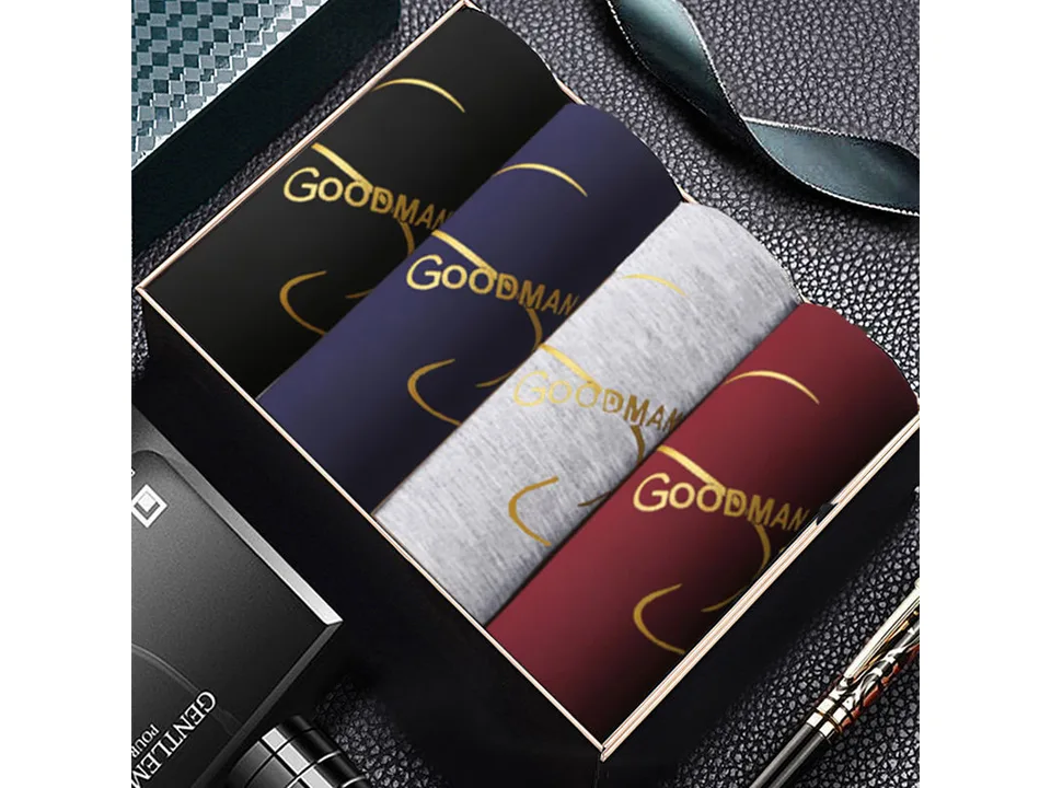 A set of four men's boxer shorts in black, navy, grey, and maroon, displayed in a gift box.