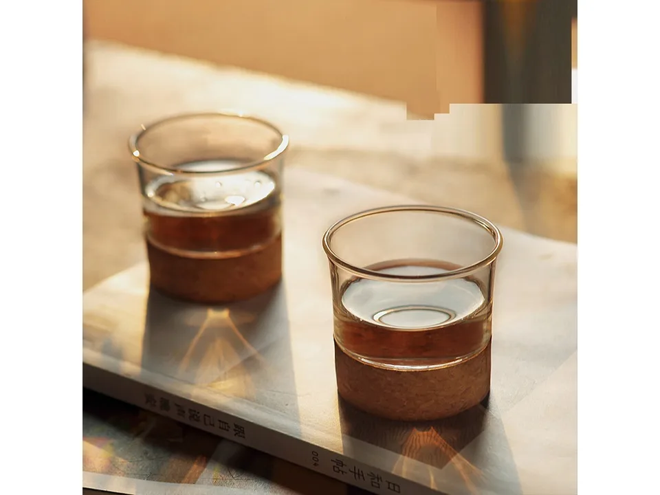 Two glass cups with cork bases filled with tea, sitting on a book.