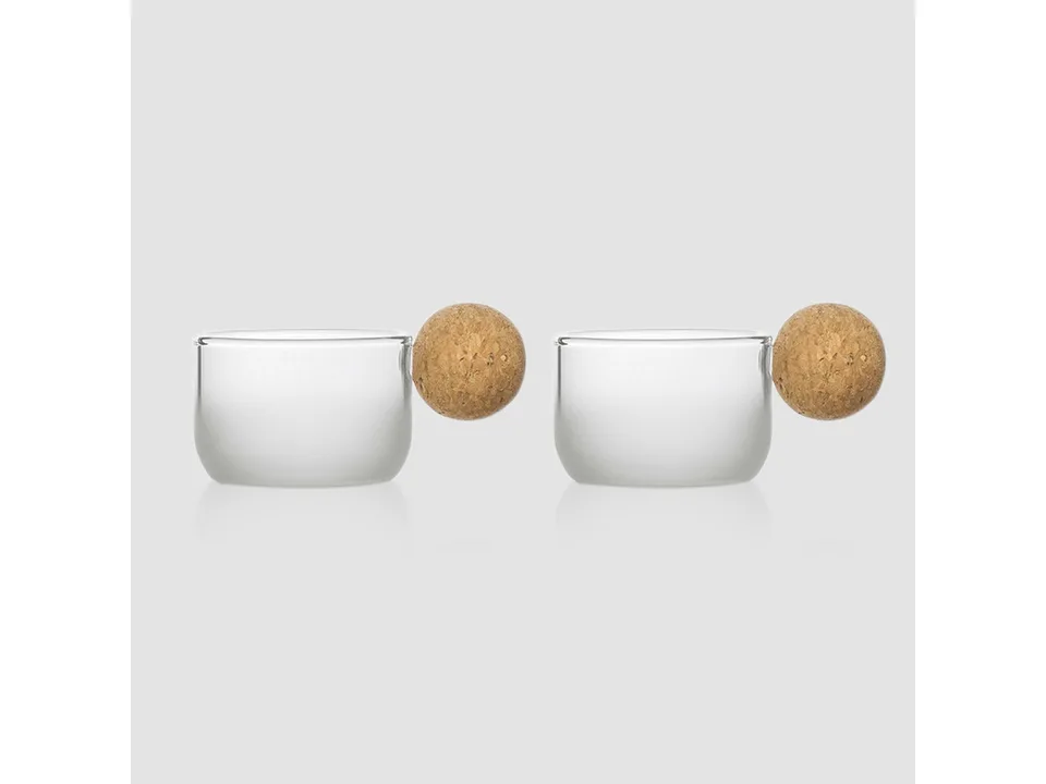 Two glass cups with round cork handles on a plain background.