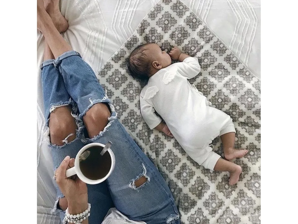 Baby wearing a white angel wing jumpsuit lying on a patterned blanket.