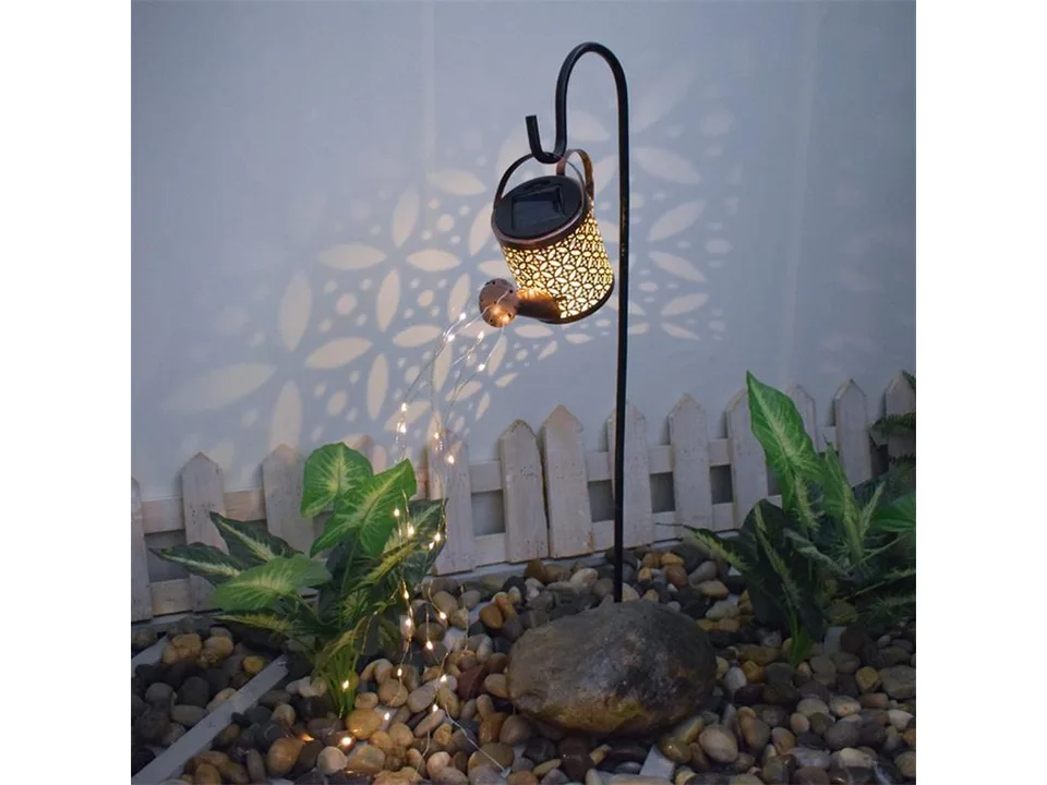 Solar watering can light glowing in a garden at night with fairy lights spilling out.