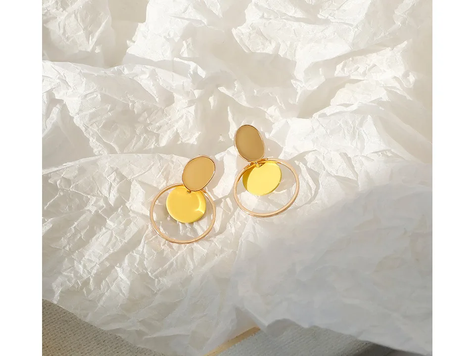 A pair of yellow and gold circular drop earrings on a white crumpled paper background.