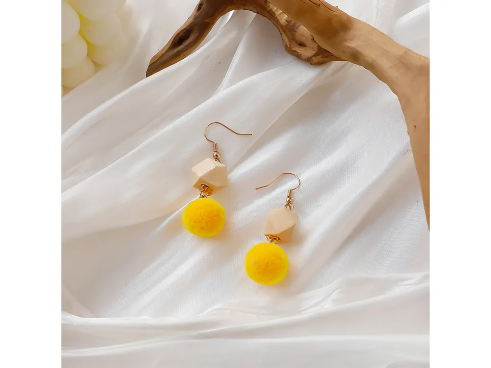 A pair of yellow pom-pom earrings with wooden beads on a white fabric background.