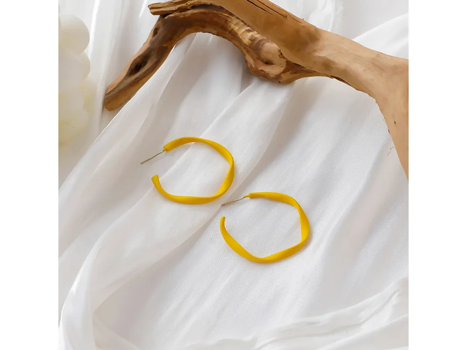 A pair of yellow hoop earrings on a white fabric background with a piece of driftwood.
