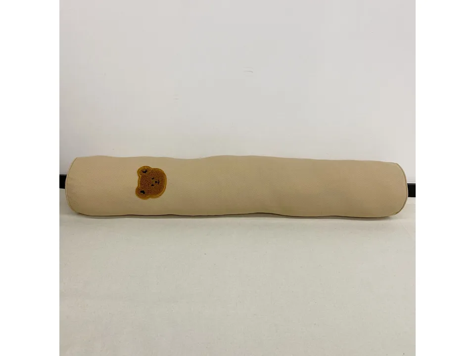 Long, cylindrical beige baby bolster pillow with a small brown bear patch.