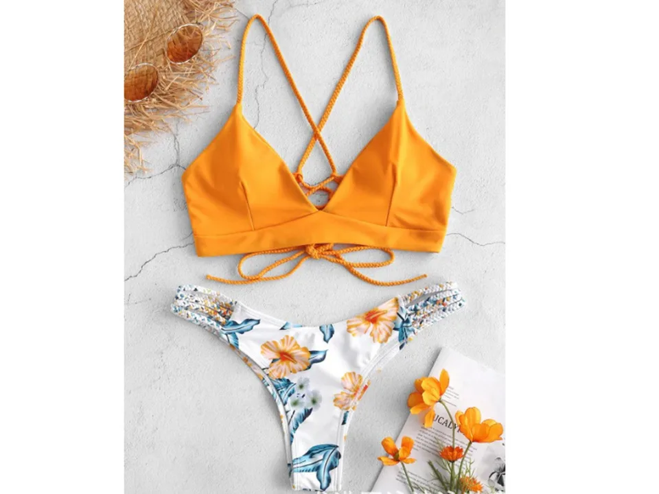 A yellow bikini top and floral print bottoms with braided straps, displayed with sunglasses and flowers.