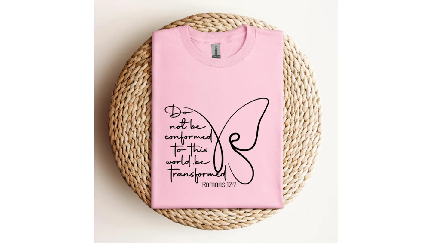A pink t-shirt with a butterfly graphic and the text 'Do not be conformed to this world be Transformed Romans 12:2'