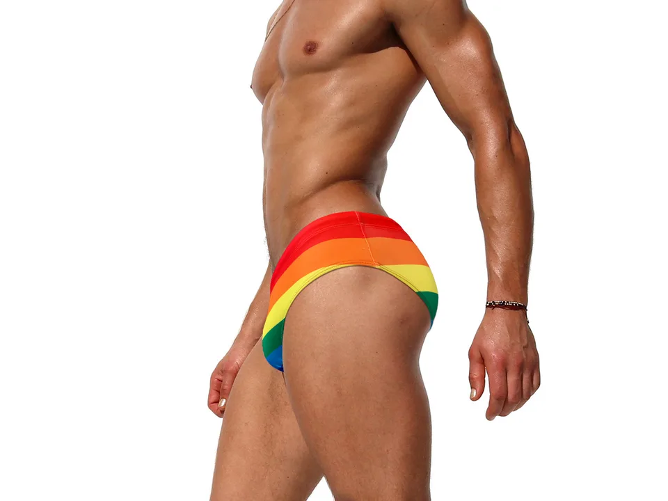 Side view of a man wearing rainbow striped swimming briefs.