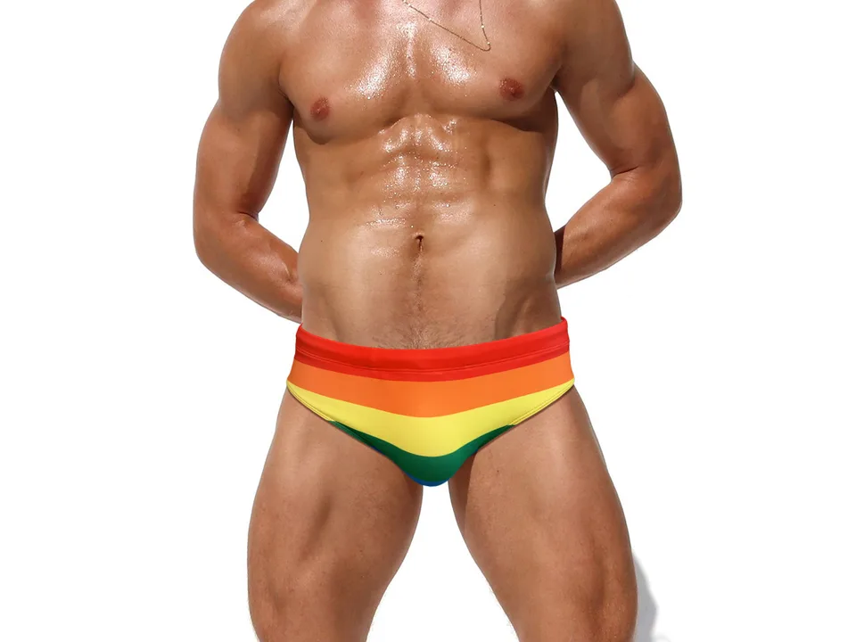 Front view of a man wearing rainbow striped swimming briefs.