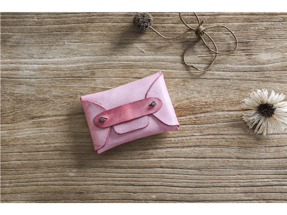 Pink leather card holder on a wooden surface with decorative dried flowers.