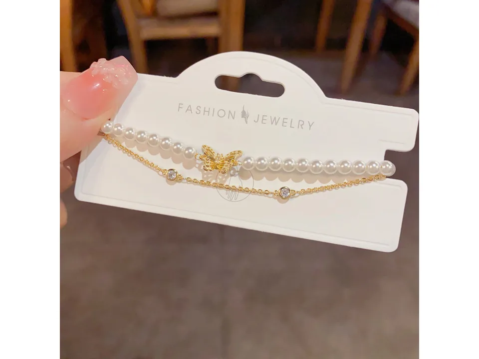 A double-layer bracelet with pearls and a gold butterfly charm on a display card.