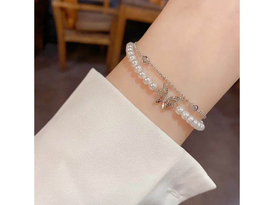 The double-layer pearl and butterfly bracelet worn on a wrist.