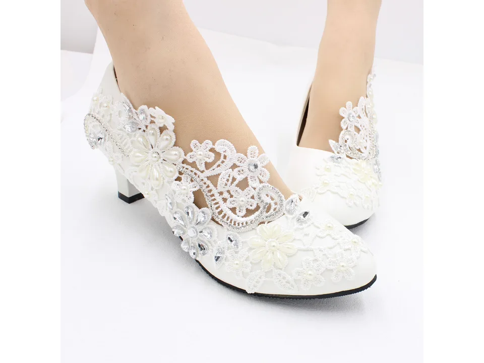 A pair of white lace bridal pumps being worn on feet.