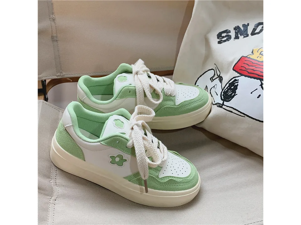 A pair of white and green casual low-top sneakers with a flower detail.