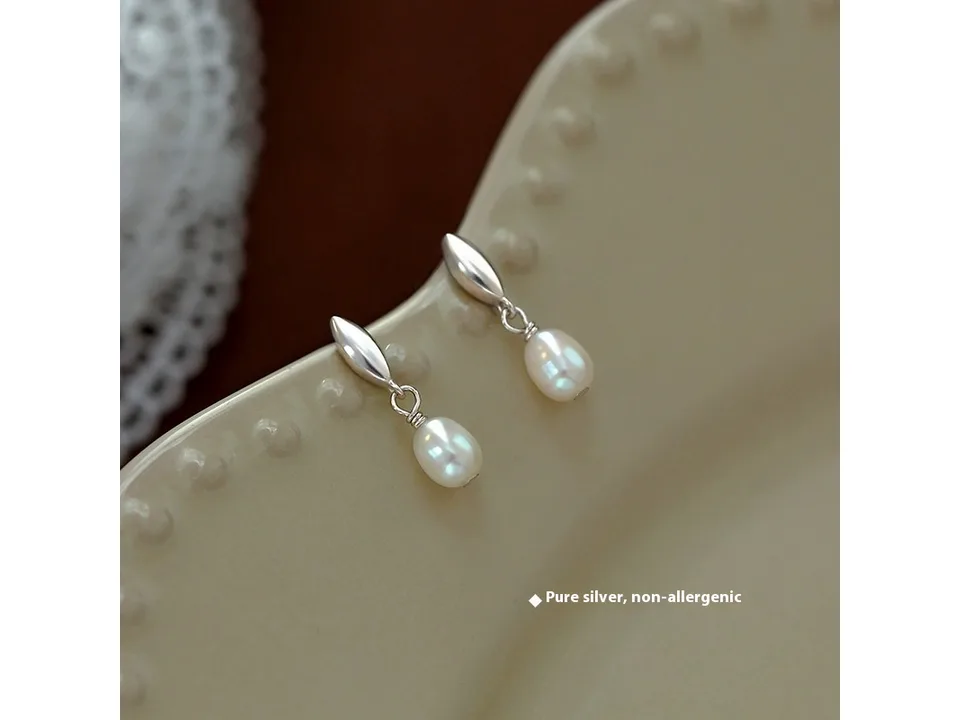 A pair of silver pearl drop earrings resting on a decorative tray.