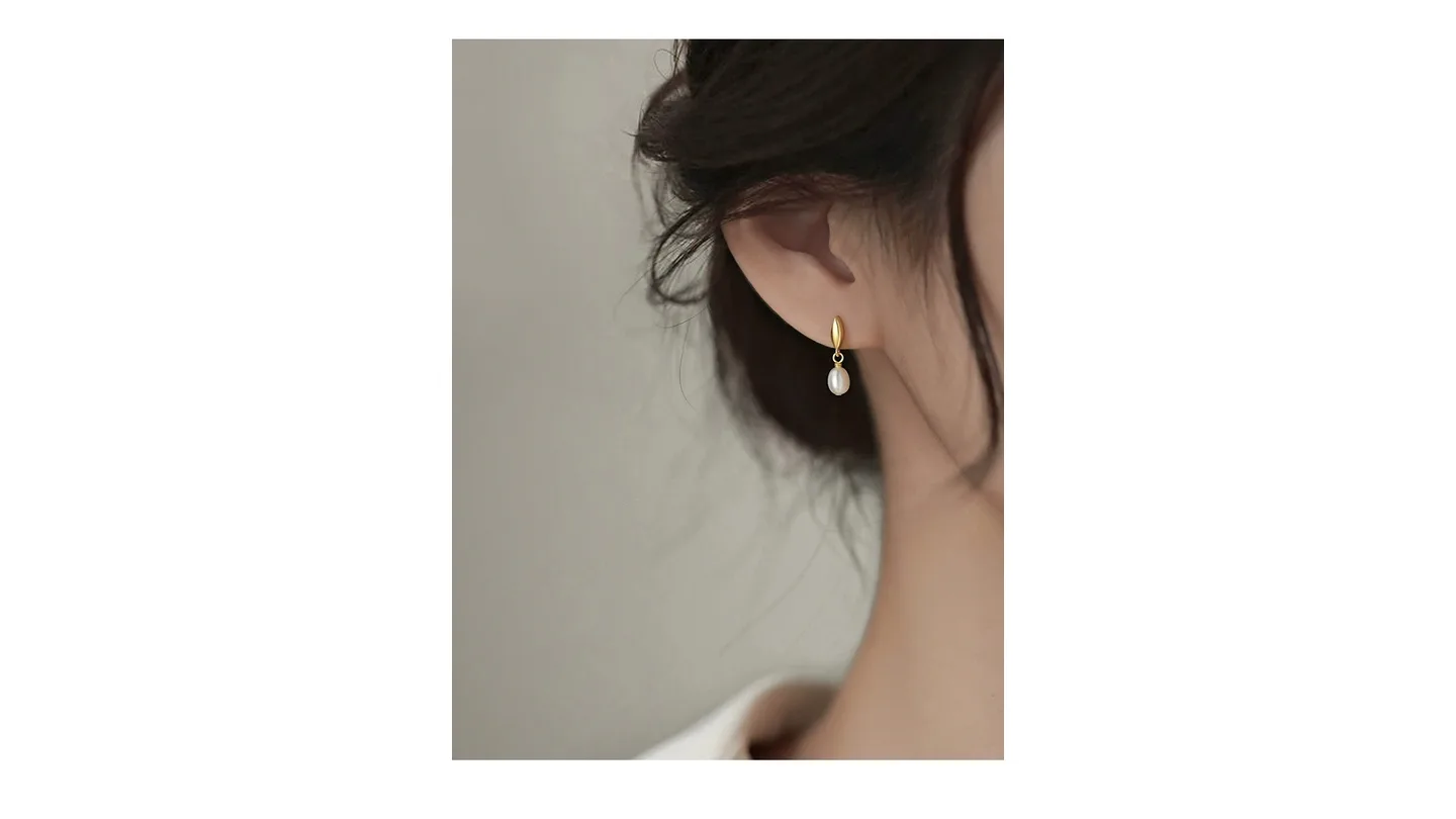 A woman wearing gold pearl drop earrings.