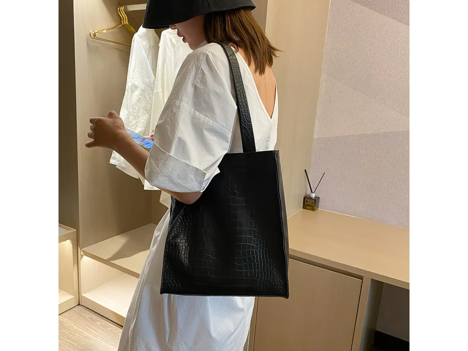 Person wearing the black crocodile pattern tote bag over their shoulder.